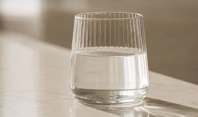 Rebrovaný pohár čistej Kangen Water® na slnkom osvetlenom pulte